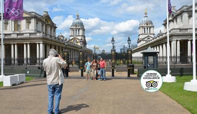 A Tour guide taking photograph of a family of four people in front of Old Royal Naval College.