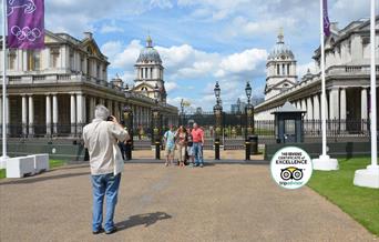 A Tour guide taking photograph of a family of four people in front of Old Royal Naval College.