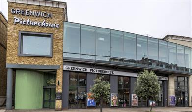 A photo of Greenwich Picturehouse from the outside .It is a modern building surrounded by film posters and two little trees.