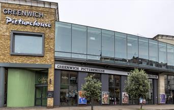 A photo of Greenwich Picturehouse from the outside .It is a modern building surrounded by film posters and two little trees.