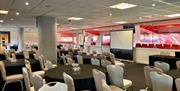 The Millennium Lounge at Charlton Athletic, a large room with multiple black tables, white chairs, business boards and an amazing view of the stadium.
