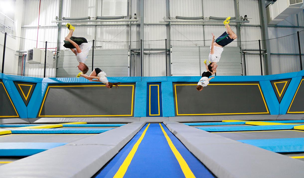 Four children in white t-shirts and black shorts jumping on the variety of interconnected trampolines.