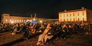People sat in front of the Queen's House on the Royal Museums Greenwich Grounds in the evening