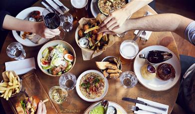 A group sit around a table full of delicious food and drink at The Admiral Hardy.