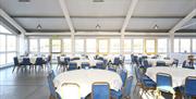 Inside the Ahoy Centre function room, showing large circular tables, blue chairs and multiple windows.