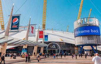 The O2 dome in white covering with 5 yellow stands visible and large glass door entrance