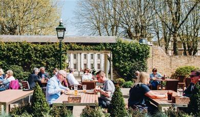 People sit for lunch and a drink in the beautiful walled garden outside The Old Brewery in the sunshine.