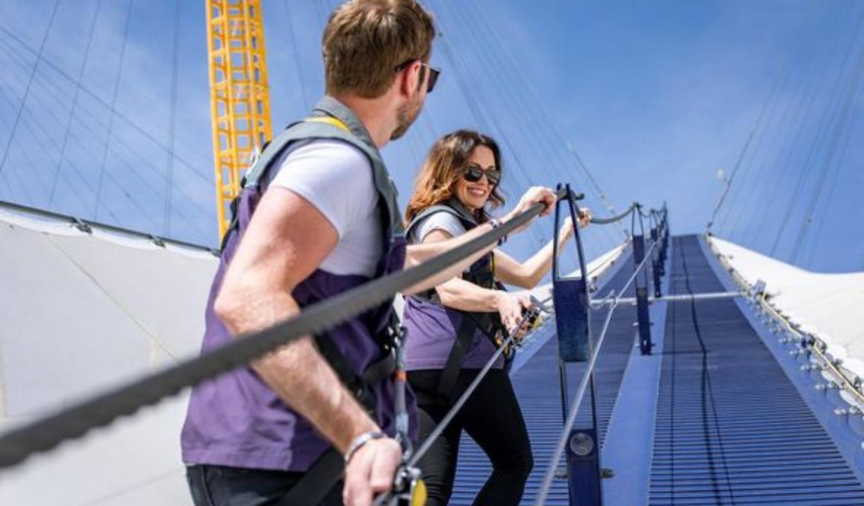 A couple climb the blue walkway of Up at The O2 on Greenwich Peninsula on a sunny, blue-skied day.