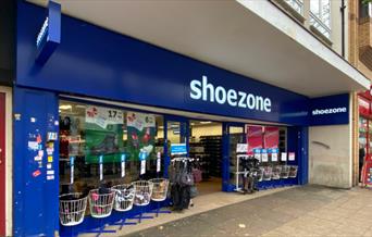 Outside Shoezone in Woolwich. A blue and white shop with shoes on display both inside and outside.