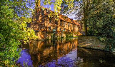 Looking over the moat at a colourful and sunny image of the Tudor Barn at Well Hall Pleasaunce Park and gardens