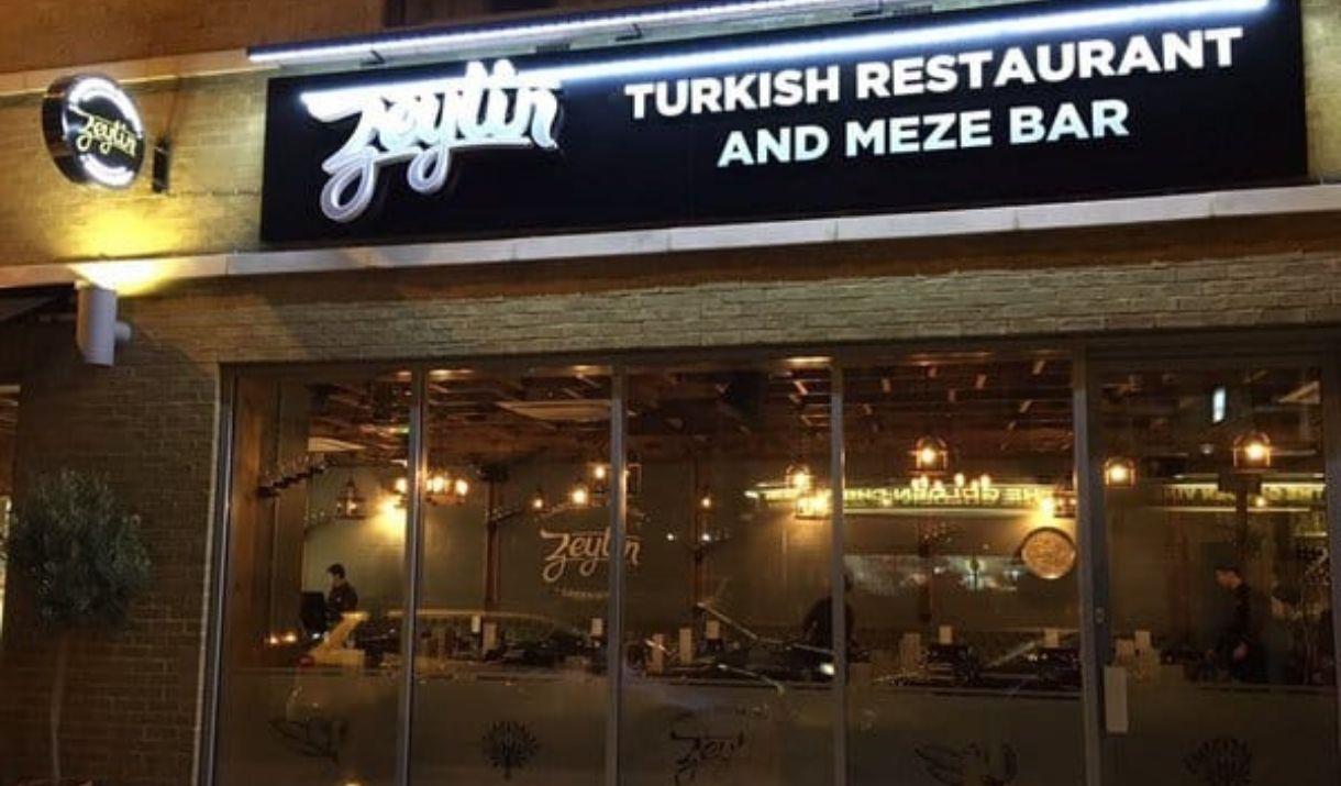 Exterior image of Zeytin Restaurant with glass entrance and warm lighting.