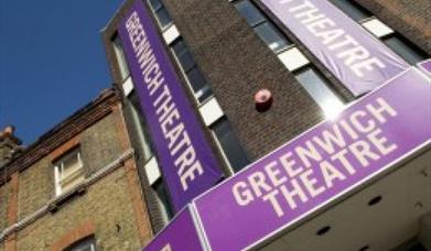 A photo taken of the Entrance to the Greenwich Theatre. it shows a brick building with three purple and white banners saying Greenwich theatre attache