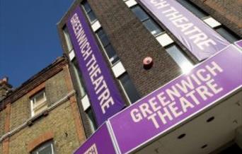 A photo taken of the Entrance to the Greenwich Theatre. it shows a brick building with three purple and white banners saying Greenwich theatre attache
